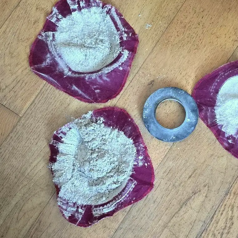 Zwei Staubfilter aus der Nähe auf einem Holzboden, daneben ein Metallring und am rechten Bildrand ein dritter Filter