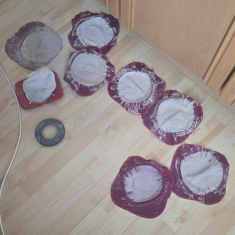 Sieben Staubfilter nach Matratzenreinigungen auf einem hellen Laminatboden, links ein Filterhalter mit eingesetztem Filter und ein Gummiring